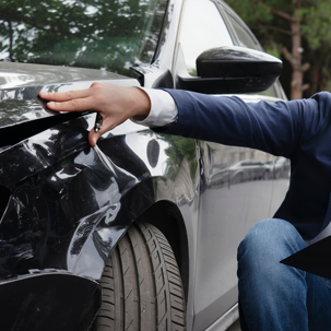 A person kneeling next to a car with a smashed in quarter panel